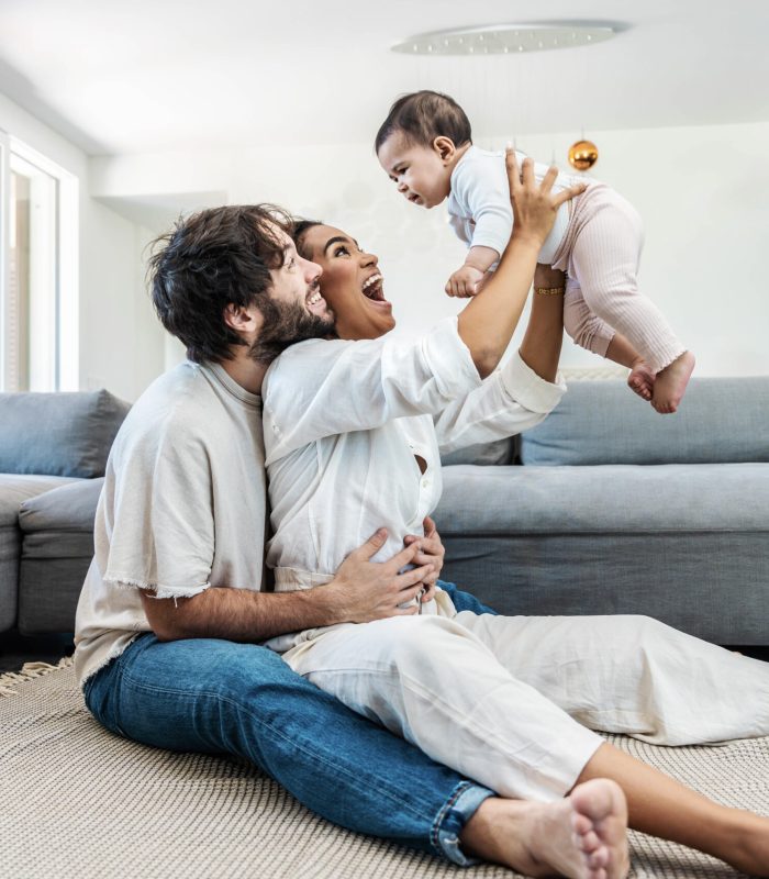 Multiracial husband and wife playing with cute little daughter at home -Cheerful parents embracing beautiful baby children indoors - Family life style concept
